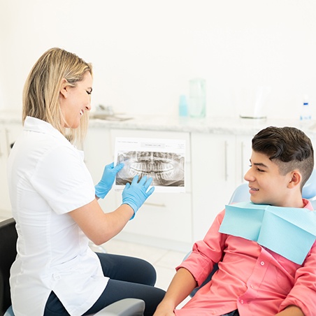 Dentist discussing symptoms with male teenager during appointment